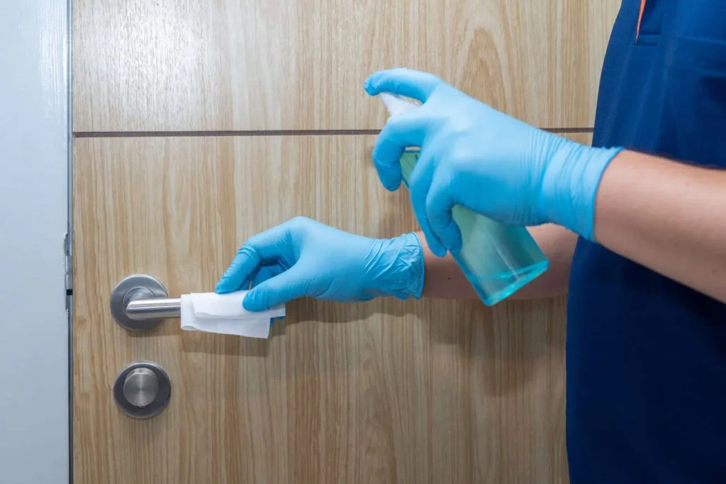 Gloved hands spraying and wiping a wood door surface during Queen City Cleaners move out cleaning in Myers Park, NC. Move Out cleaning near me