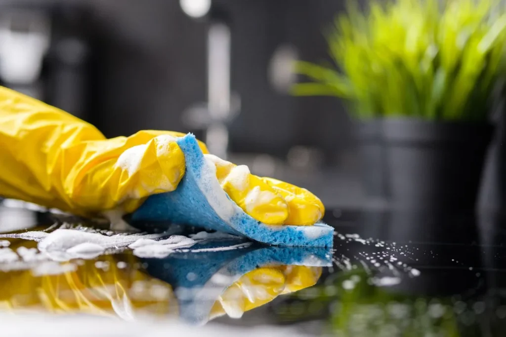 Yellow-gloved hand scrubbing a glossy surface with a sponge during Queen City Cleaners move out cleaning in Eastover, NC. Move Out cleaning near me